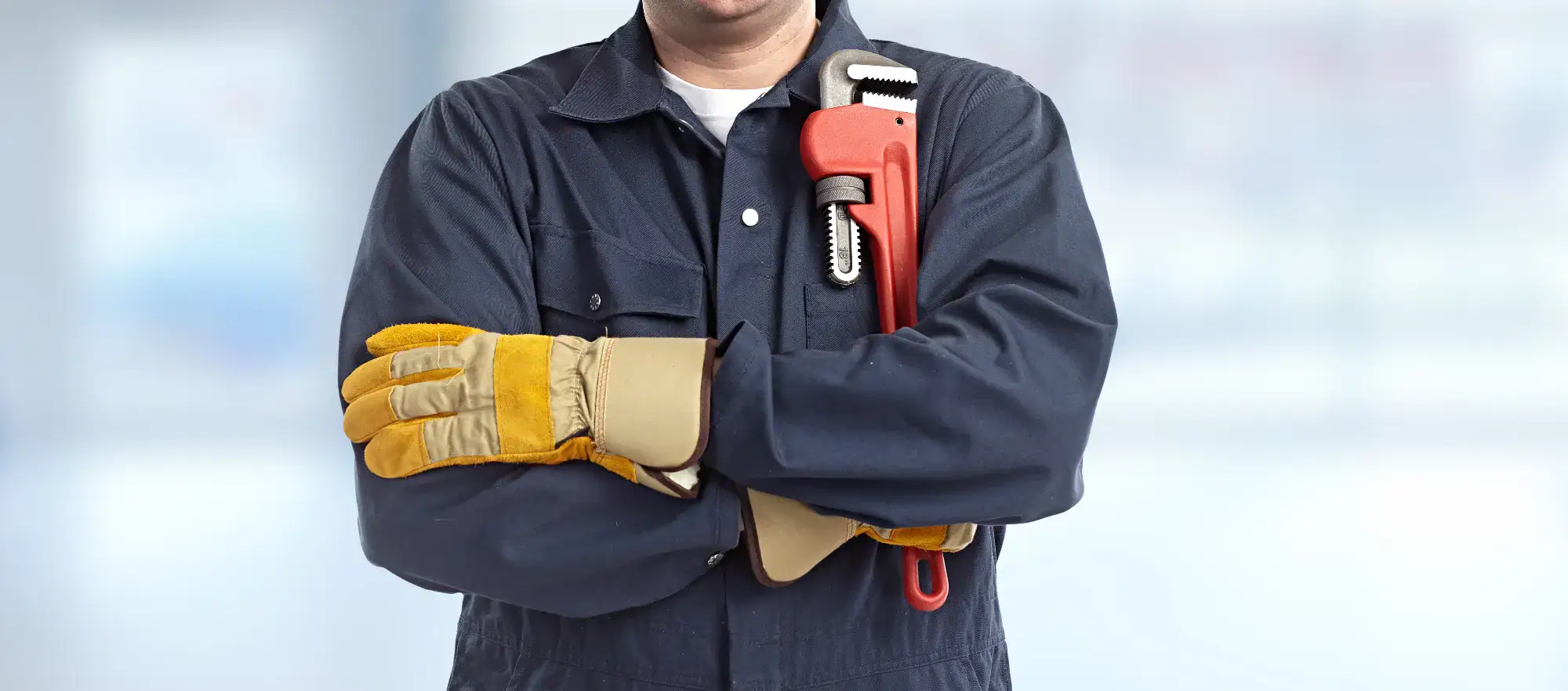 Man in a blue uniform, holding a wrench, standing confidently in a residential setting in Bergen County, NJ. The background shows suburban homes, with greenery and a clear sky. The man appears focused and ready to tackle a home repair, showcasing expertise and professionalism in his trade.
