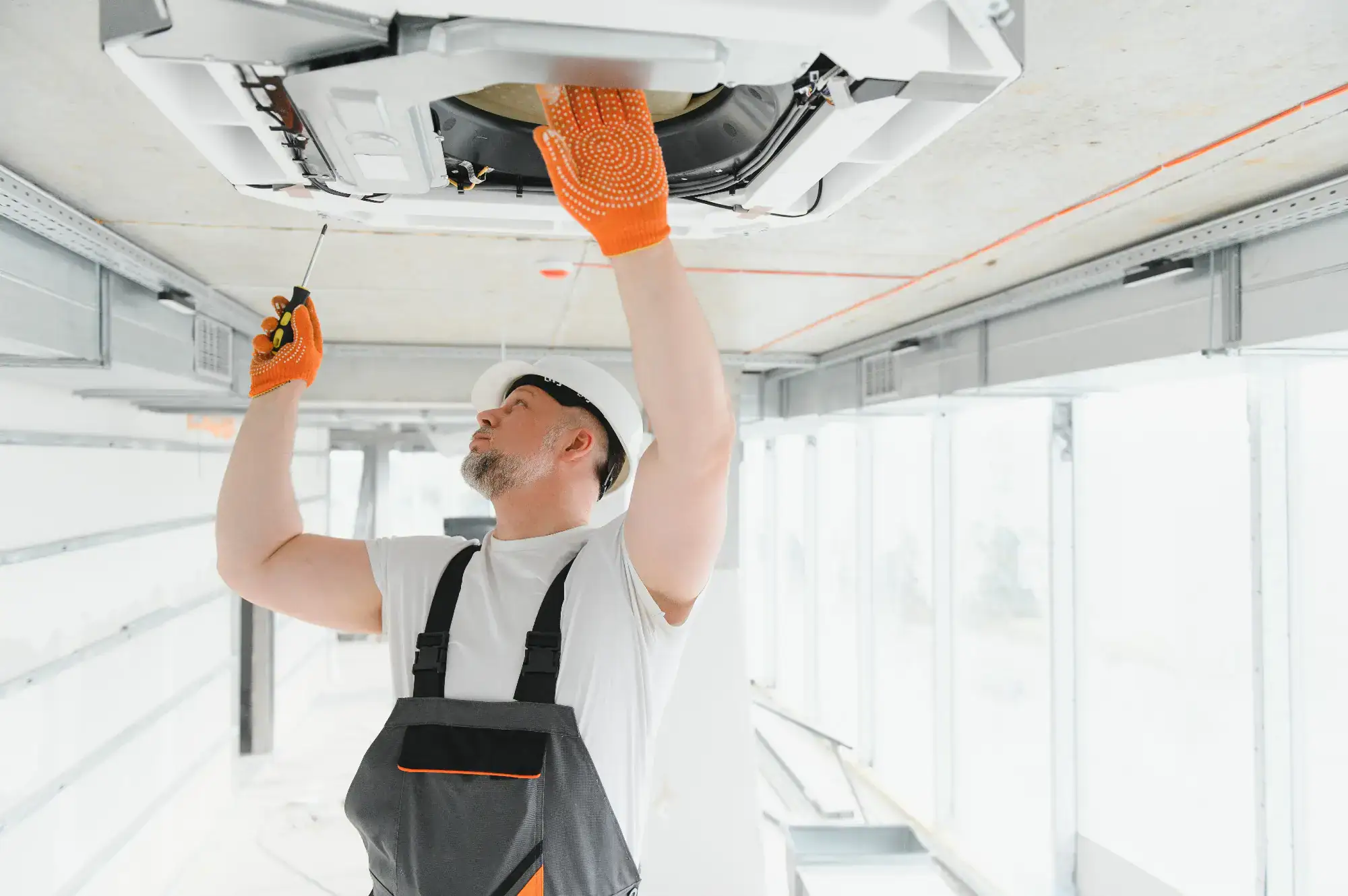 An experienced handyman in overalls and safety glasses is diligently repairing a ceiling fan in a home in Bergen County, NJ. The room features warm, natural lighting, and the handyman is carefully inspecting the fan blades while standing on a ladder, ensuring the repair is done with precision and safety.