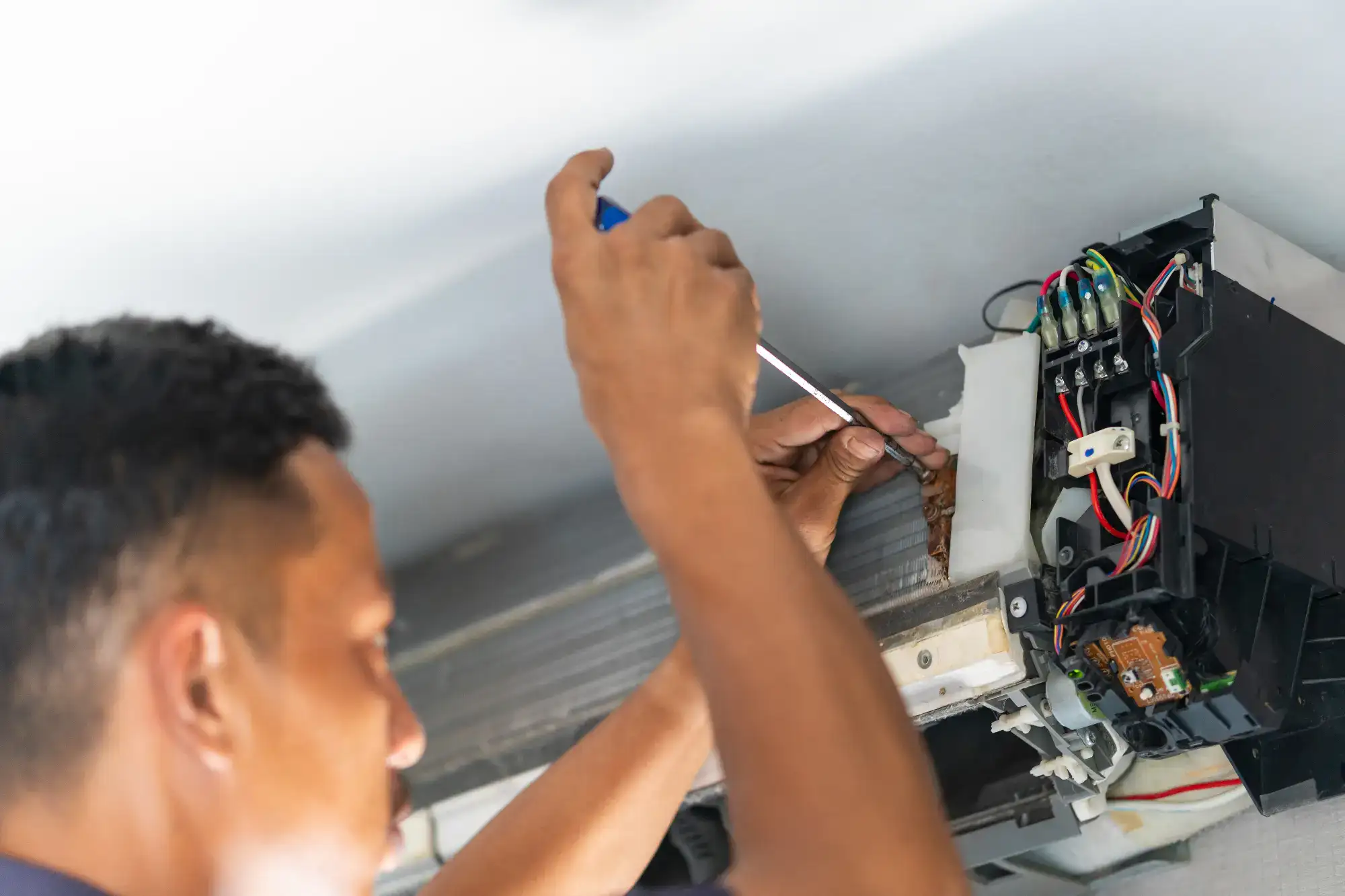 A technician is repairing an air conditioner in a home in Bergen County, NJ. He is wearing a blue uniform, using a wrench to adjust the unit, with tools and parts laid out nearby. The room is bright, and the technician is focused on ensuring the AC runs efficiently for the homeowners