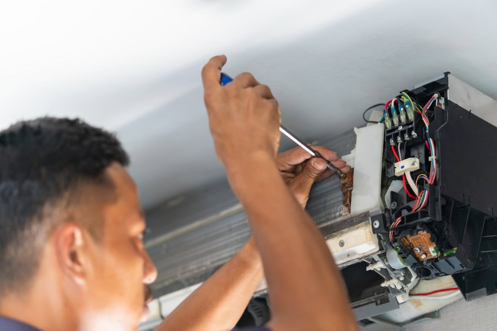 An HVAC technician is servicing the internal components of a mini-split air conditioning unit.